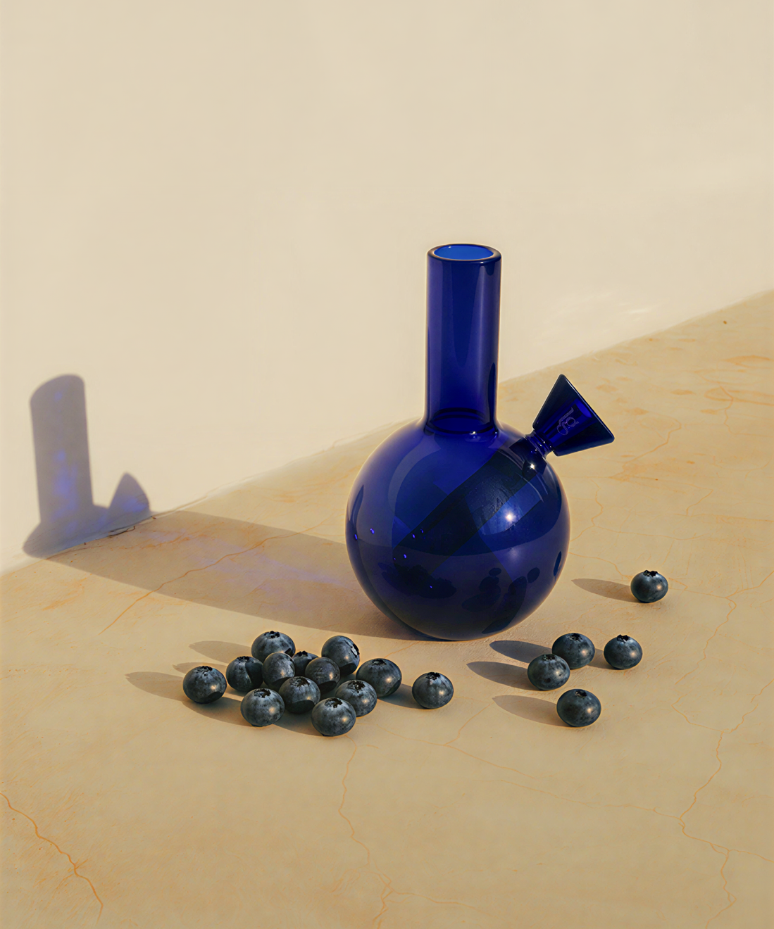 Blue glass vase with a unique design on a beige surface with blueberries around it.