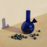 Blue glass vase with a unique design on a beige surface with blueberries around it.