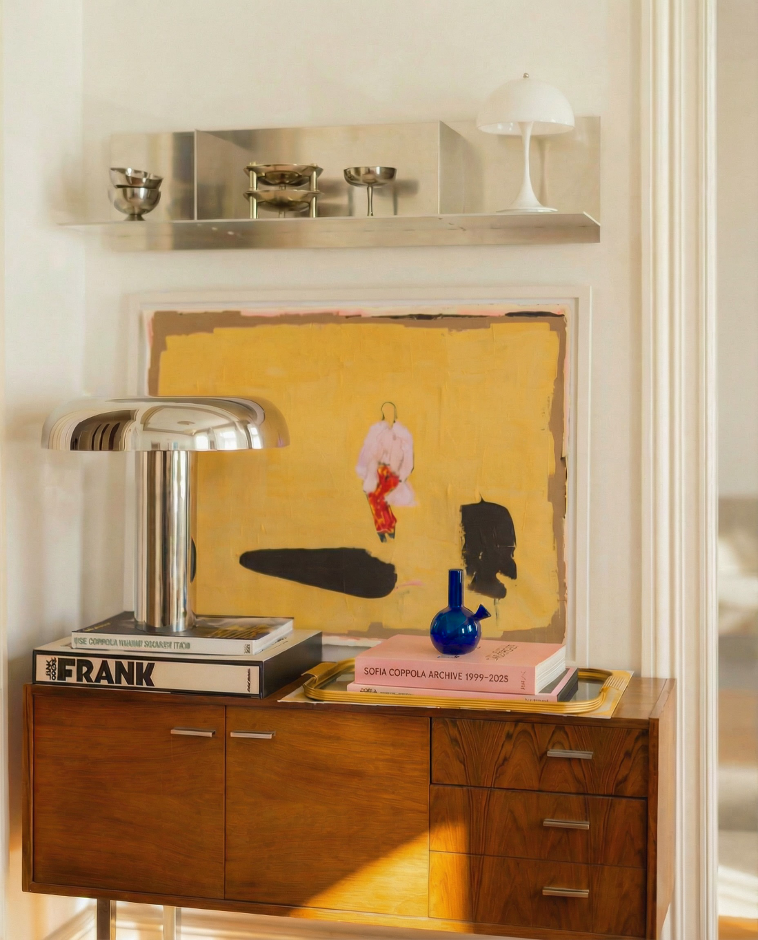 loke glass gaia in blue on Wooden console table with a yellow artwork, books, and decorative items.