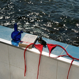 loke glass gaia in bvlue next to Red bikini straps, blue bottle, and book on a ledge with water in the background