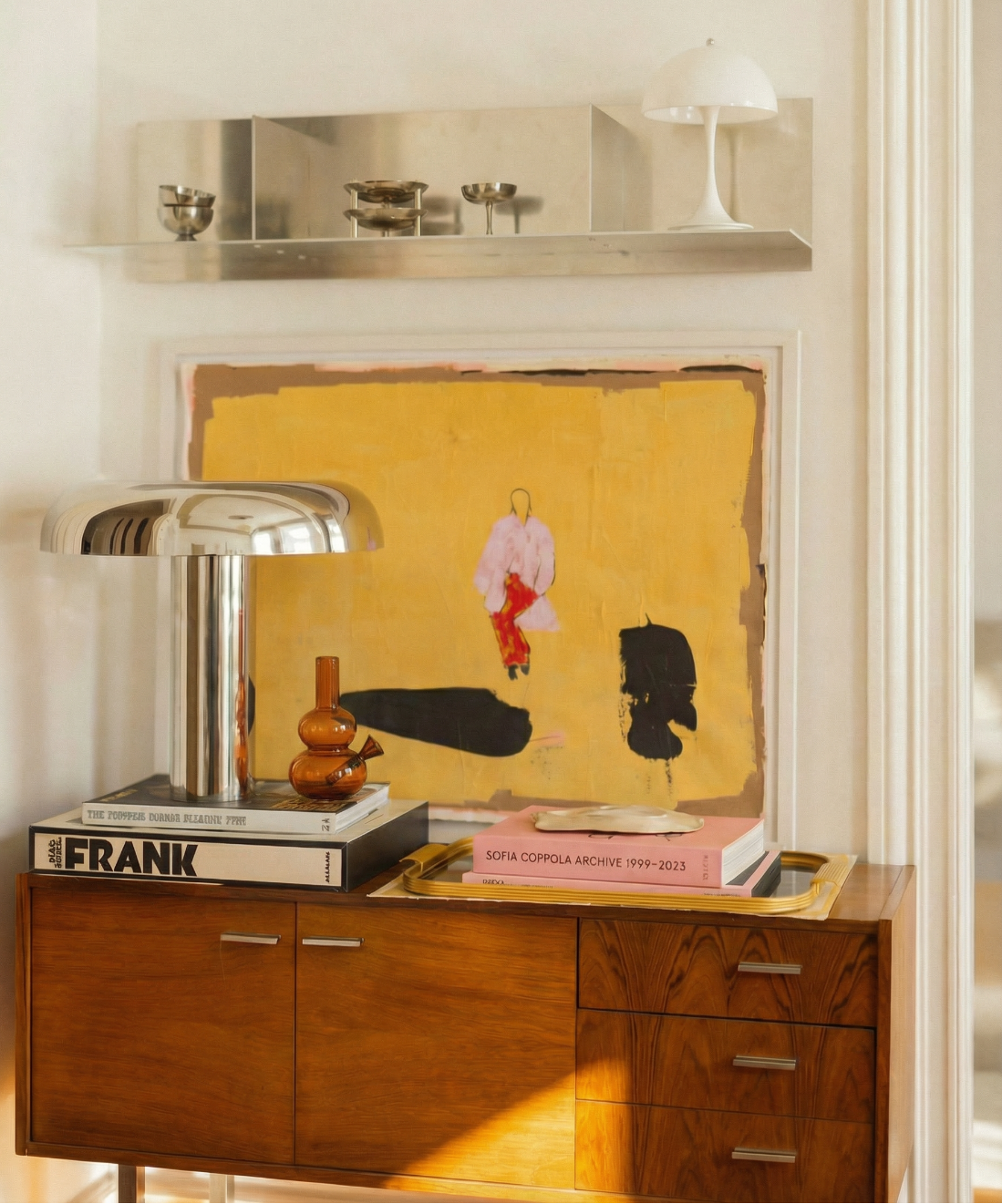 loke glass lilah in amber on Wooden sideboard with books, a lamp, and a painting on a white wall.