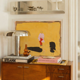 loke glass lilah in amber on Wooden sideboard with books, a lamp, and a painting on a white wall.